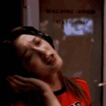 a woman wearing headphones and a red shirt is standing in front of a machine .