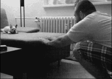 a man is kneeling down next to a couch with a dog laying on it .