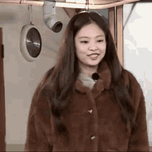 a woman in a fur coat is standing in a room with a clock hanging on the wall .
