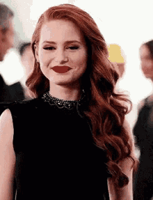 a woman with red hair and red lipstick is wearing a black dress and a necklace .