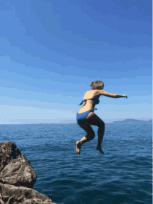 a woman in a blue bikini jumping into the ocean