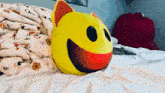 a stuffed smiley face is laying on a bed with a blanket