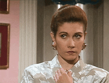 a woman wearing a floral shirt and earrings looks at the camera with voyager in the corner