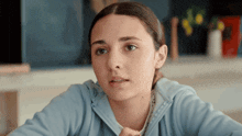 a young girl in a blue sweatshirt is sitting at a table and looking at the camera