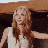 a woman with long blonde hair is wearing a white tank top and standing in a room .