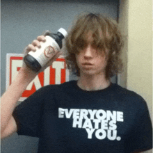 a man wearing a shirt that says everyone hates you holds a bottle