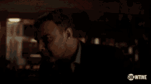 a man in a suit is standing in a dark room with showtime written on the bottom of the screen .