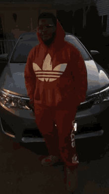 a man in a red adidas hoodie is standing in front of a car