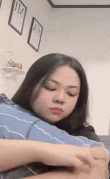a woman is sitting on a couch with her eyes closed and holding a blue pillow .