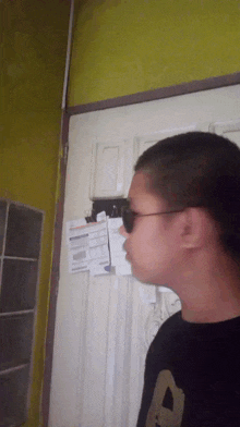a man wearing sunglasses and a shirt with the letter a on it stands in front of a door