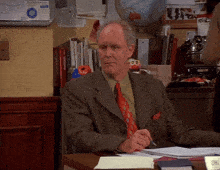 a man in a suit and tie sits at a desk in front of a bulletin board that says " new york times "