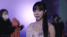 a woman wearing a white dress and a necklace is standing in front of a purple background .