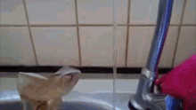 a faucet is running water into a sink with a pink bag in the background