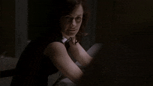 a woman in a black shirt with a white collar sits in a dark room