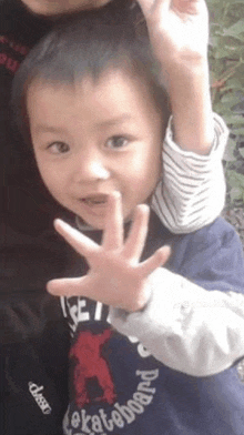 a young boy wearing a shirt that says skateboard is giving the peace sign