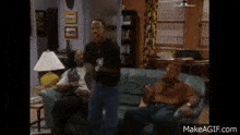 three men are sitting on a couch in a living room and one of them is dancing .