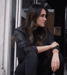 a woman wearing a black jacket and black jeans sits on a doorstep