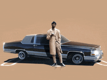 a man in a trench coat stands in front of a low rider car