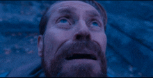 a man with a beard and blue eyes looks up at something