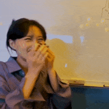 a woman is laughing while covering her mouth with her hands in front of a white board .