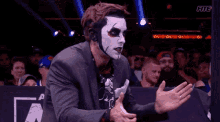 a man wearing a mask and a suit is standing in front of a crowd of people .