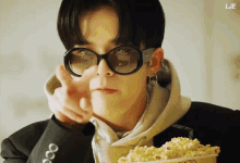 a man wearing sunglasses is holding a bowl of popcorn and pointing