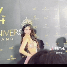 a woman wearing a crown stands in front of a wall that says miss universe and mgi