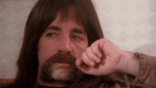 a man with long hair and a beard has his hand on his chin