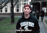 a woman wearing a michigan state sweatshirt is standing on a sidewalk .