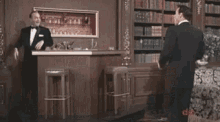 a man in a tuxedo stands in front of a bar