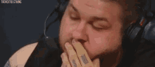 a man with headphones on is covering his mouth with his hands .