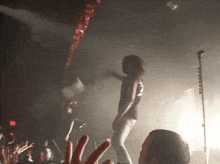 a woman stands on a stage in front of a microphone with a crowd watching