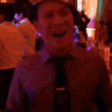 a man in a suit and tie is dancing in a room with purple lights behind him .
