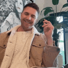 a man wearing a tan jacket is smiling in front of a picture of a girl
