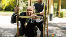 a man in a suit is pushing a cart with the nbc logo in the corner