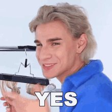 a man in a blue shirt is smiling and holding a hanger with the word yes in white letters