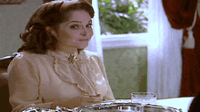 a woman sits at a table with a glass of water in front of her