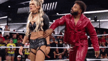 a man and a woman are standing in a wrestling ring . the man is wearing a red leather jacket .