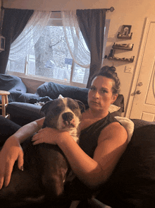 a woman sits on a couch holding a large dog