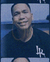 a man wearing a black shirt with the letter lx on it is smiling