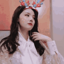 a woman wearing a headband with reindeer antlers looks at the camera