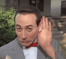 a man in a suit and bow tie is covering his ear with his hand