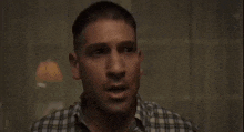 a man in a plaid shirt is sitting in a dark room