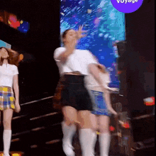 a group of women are dancing on a stage in front of a sign that says voyage .
