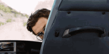 a man wearing glasses looks out from behind a car seat
