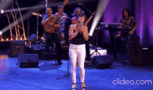 a woman singing into a microphone with a band behind her and a clipeo.com logo in the corner