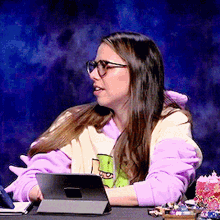 a woman wearing glasses is sitting at a desk with a tablet in front of her