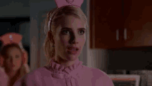 a woman wearing a pink dress and a pink crown is standing in a kitchen .