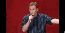 a man is holding a microphone in front of a red curtain while standing on a stage .