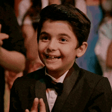 a young boy wearing a tuxedo and bow tie is smiling and clapping